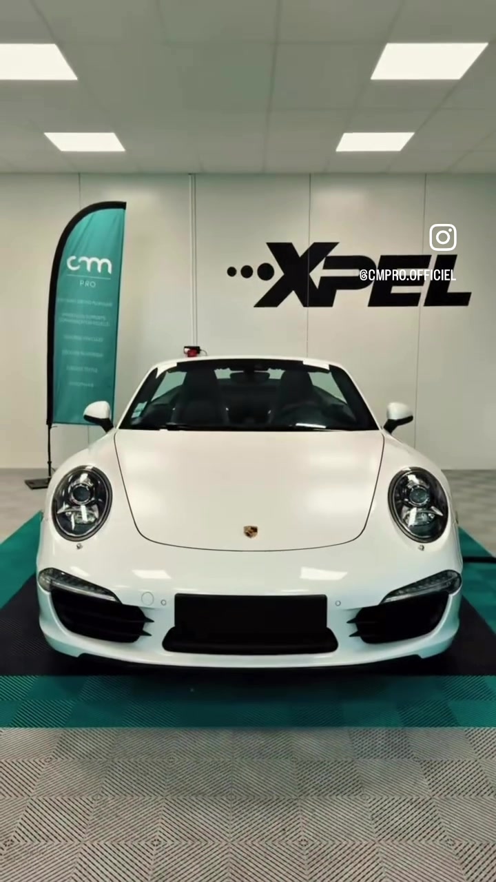 Porsche blanche de face dans l’atelier CMPRO, devant le logo XPEL