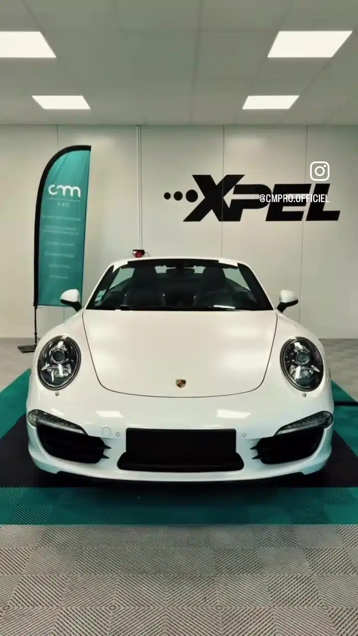 Porsche blanche de face dans l’atelier CMPRO, devant le logo XPEL